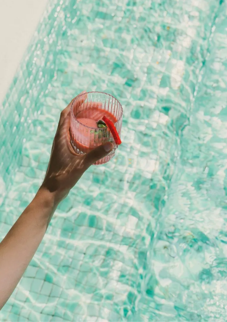 Mano sosteniendo un cóctel sobre el agua de la piscina