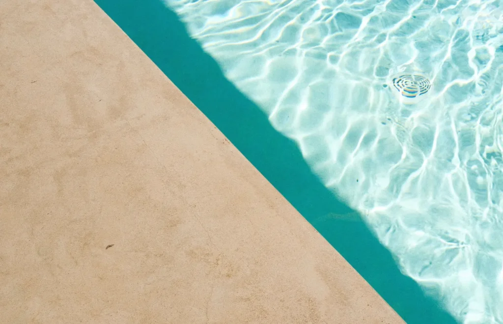 Vista cenital del borde de una piscina: una línea recta de sombra separa el agua en penumbra a la izquierda del agua iluminada por el sol a la derecha