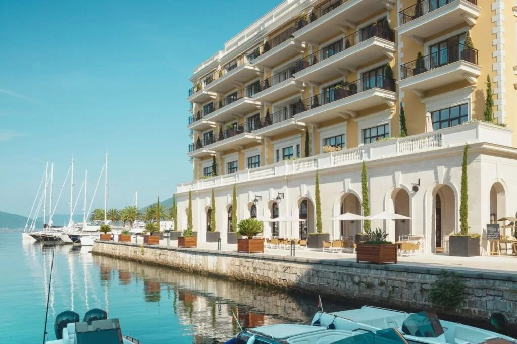 Fachada de un hotel junto al agua, con veleros amarrados en el muelle en primer término