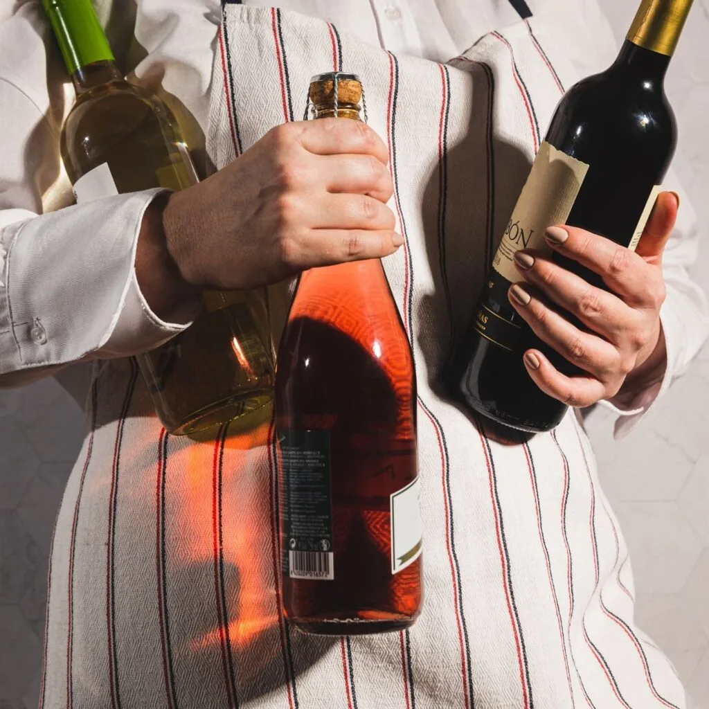 Un sumiller sostiene tres botellas de vino con sus etiquetas a la vista, apoyadas sobre un paño de rayas